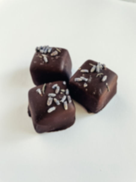Dark chocolate enrobed cherry lavender caramel squares with dried lavendar sprinkled on top, sitting on a white background