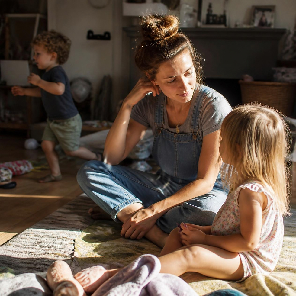 A mother basks in a warm patch of sunlight, sharing a moment with her daughter, while playful energy swirls around them.