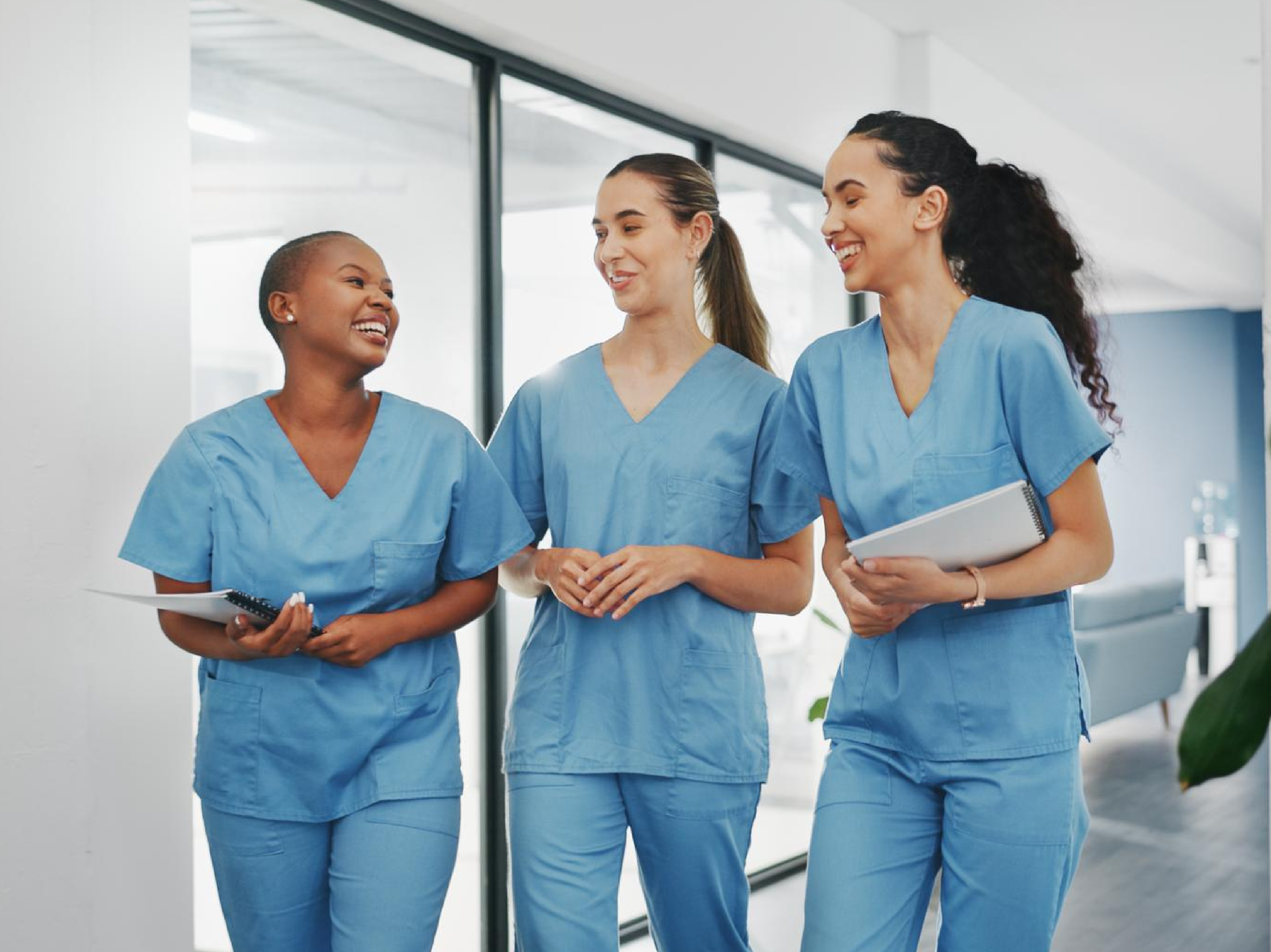 Three nurses in scrubs discussing NMC registration process for UK nursing practice