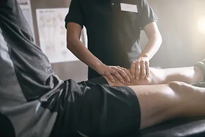 A doctor examining a patient's knee while the patient sits on the examining table.