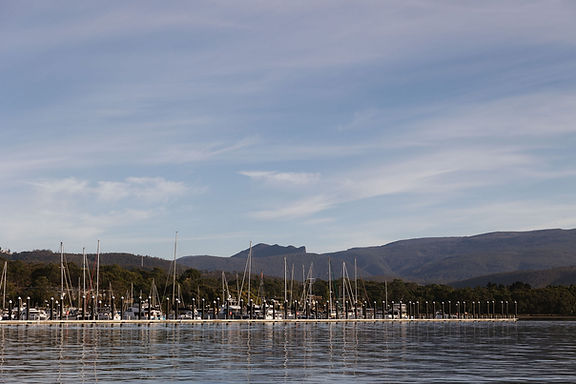 View of Margate Marina on calm water with boats, forested hills and kunanyi / Mount Wellington in the background.