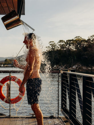 Guest cooling off with the shower bucket on the deck after a KUUMA sauna session.