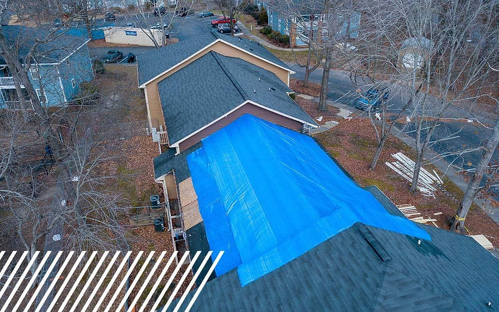 A house with a blue tarp covering part of the roof in a residential area with leafless trees. Supplies and a yard visible in the background.