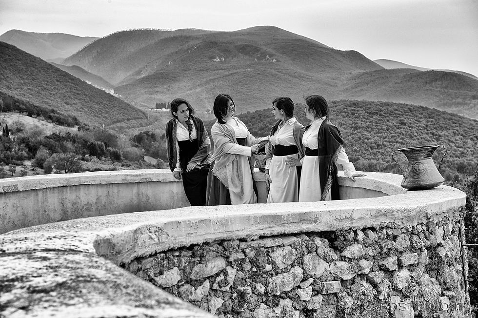 Foto in bianco e nero di un gruppo di donne in abiti antichi sul torrione di un paese medioevale i