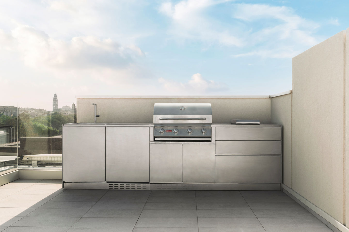 Stainless steel outdoor modular kitchen with built in gas grill and side prep area, photographed on a modern rooftop terrace.