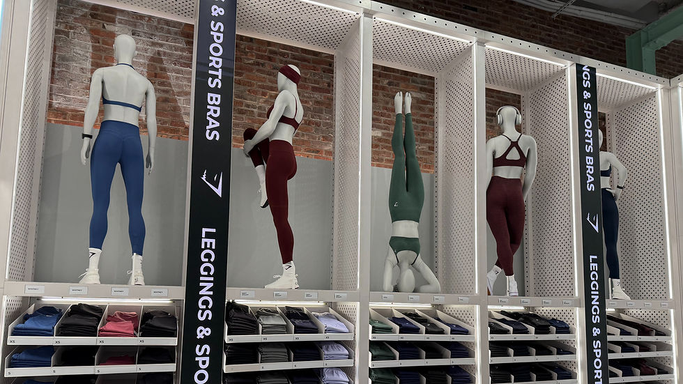 At Gymshark in NYC. Mannequins in activewear pose against a brick wall in a store. Text reads "Leggings & Sports Bras." Stacked shelves with folded apparel.