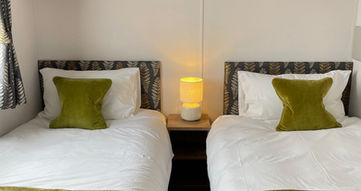 A single bed on each side of the room, normal single beds, with overhead storage and a window on the left hand side of the room.