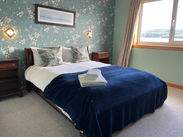 Spacious room with flower wallpaper, two bedside tables with mural lights on each side and a double window with long curtains on the side. White linen on the bed along with cushions, throw and bath and hand towels.