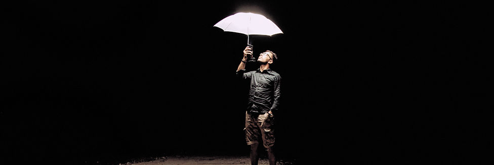 Homem narcisista, está com guarda-chuva branco num palco escuro, chão está gasto e ele olha para cima preocupado