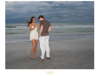 Man and Woman on beach looking at engagement ring on a windy night