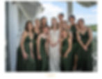 A bride in a white gown surrounded by bridesmaids in green dresses, smiling on a balcony. Blue sky and greenery in the background.