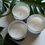 Thumbnail: Three white candles on white surface with green leaves Maddox Candles