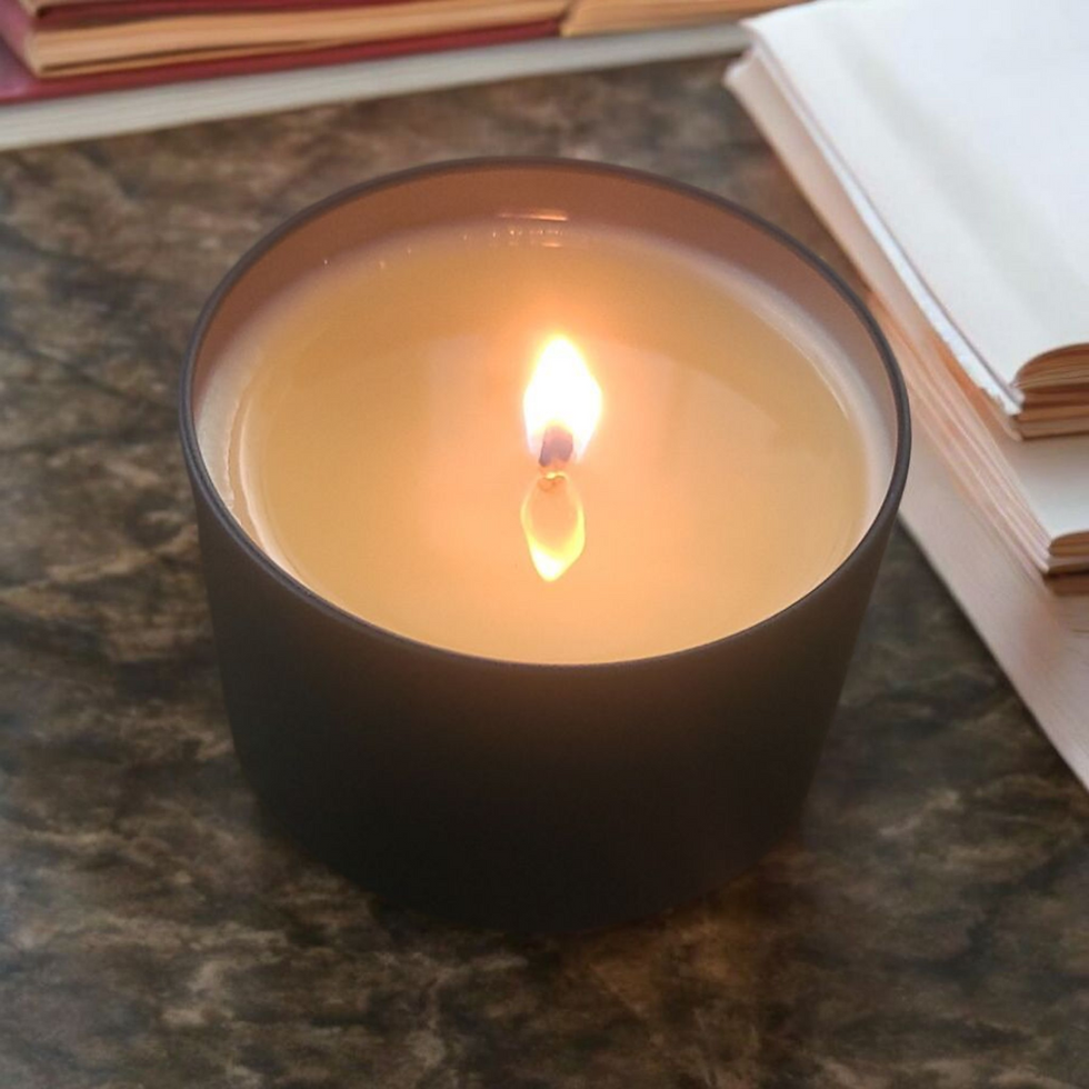 Lit candle in black container with a bright flame, Maddox Candles.