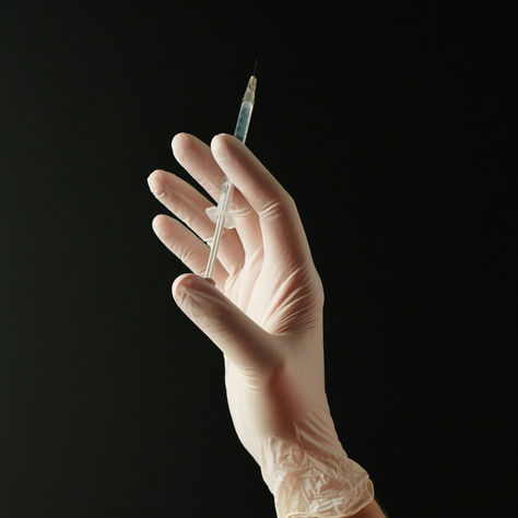 Gloved hand holding a used NAD+ injection needle and syringe, ready for safe sharps bin disposal