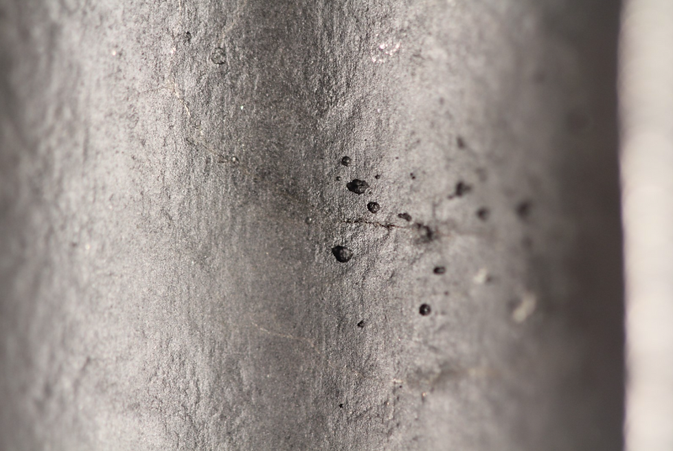Nahaufnahme von Lochfraß an einer Metalloberfläche, verursacht durch mikrobielle Aktivität.