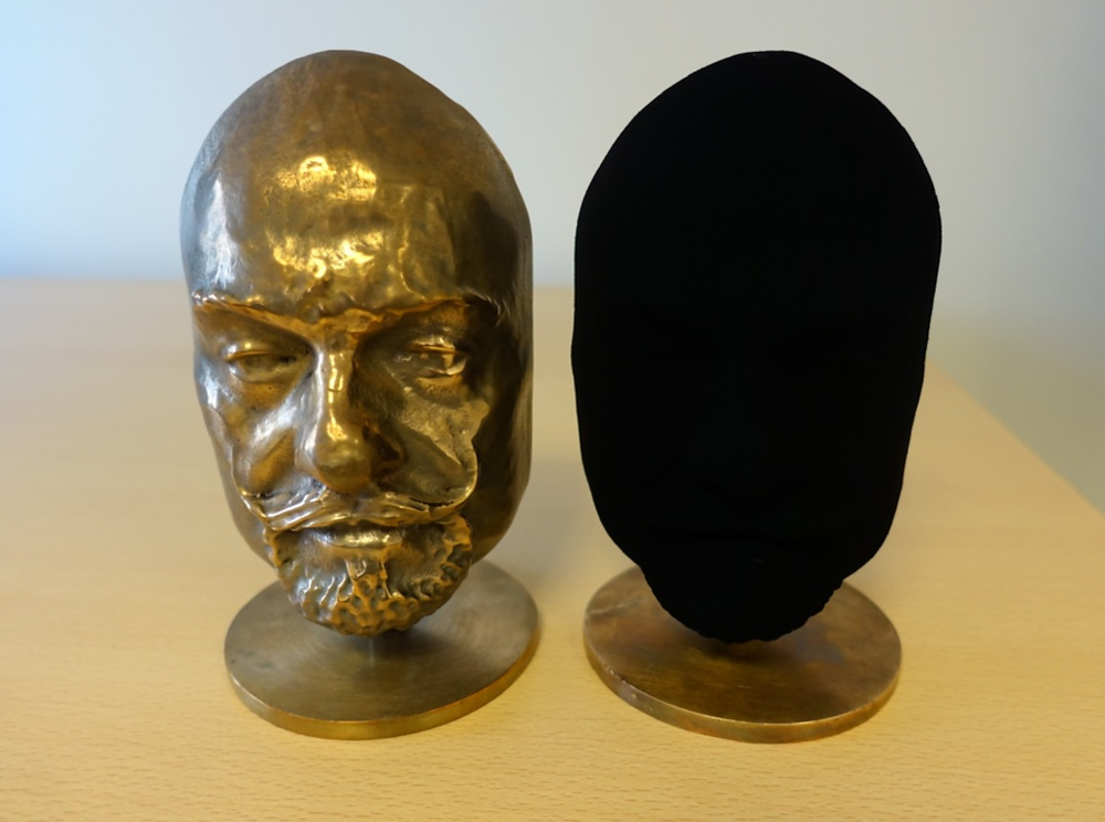 two heads made of brass, one is left untouched while the other is painted in vantablack