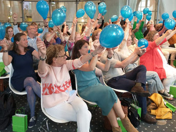 Deelnemers houden blauwe ballonnen omhoog tijdens een interactieve werkvorm van Groeibrein