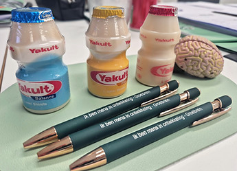 Yakult flesjes, Groeibrein pennen met tekst Ik ben mens in ontwikkeling en een hersenenmodel op tafel