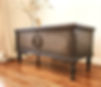 Antique chest with intricate woodworking refinished in Honfluer chalk paint and black wax and staged with a vase filled with wheat stems and a bottle of Vodka.