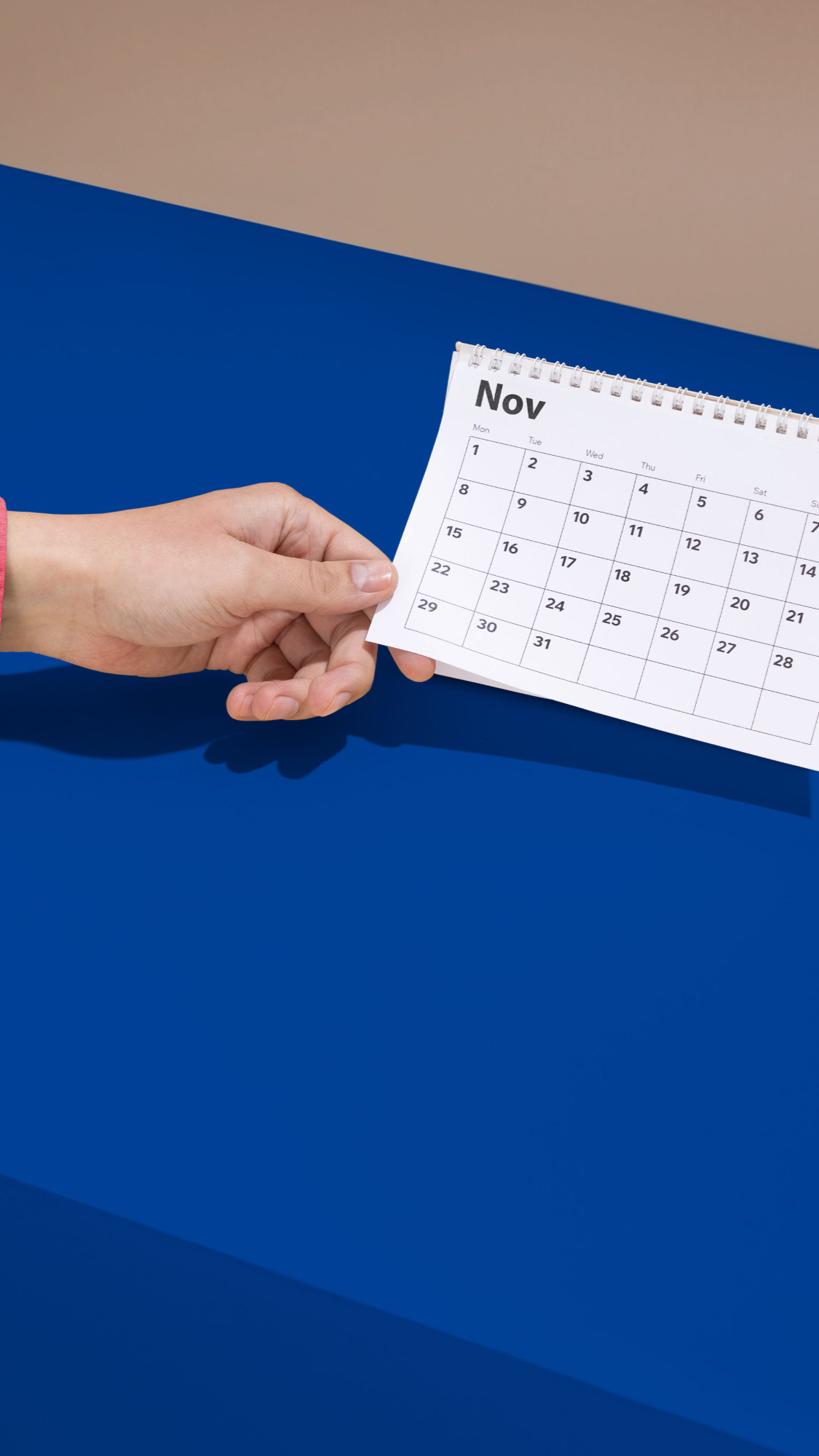 Hand holding a desk calendar open to November on a blue background
