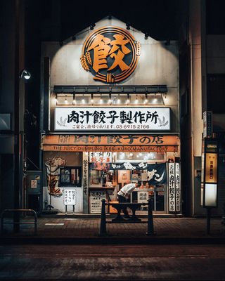 A nighttime scene of a bustling dumpling restaurant in Tokyo. The illuminated sign "Juicy Dumplings" stands out in the quiet street, showcasing the iconic dumpling image. The warm lights and cozy atmosphere make this Tokyo restaurant a local favorite. NFT Photography by Tokyo Photographer Deniz Demir. Tokyo, Japan.