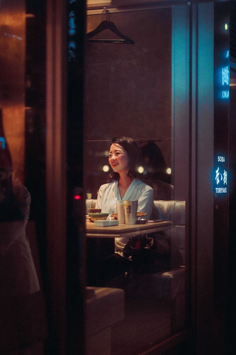 A Japanese woman smiling at a bar in Tokyo, with dim lighting and the lively atmosphere of the bar around her.