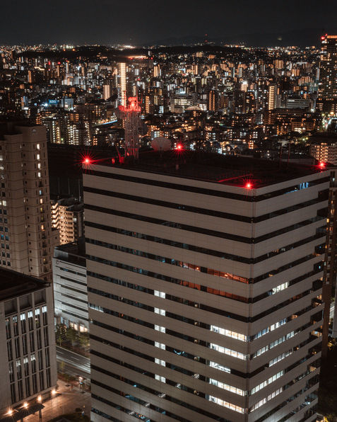A stunning night view of the cityscape of Tokyo, with glowing skyscrapers and bustling city lights. The foreground showcases a tall building with red lights on top, while the background reveals a network of illuminated buildings stretching across the horizon. The city is alive with vibrant lights, creating a dynamic contrast of shadows and brightness. This captivating scene captures the essence of Tokyo’s nightlife and urban beauty. Photographer Deniz Demir, Japan. Tekumi Studios.





