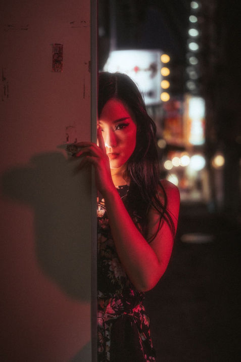 A model peeking into the camera with city lights in the background, her half face hidden behind a door, creating a mysterious and intimate vibe.







