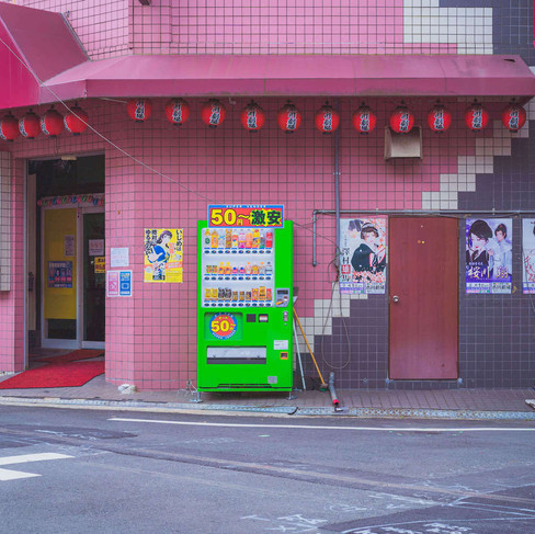 A green vending machine and a building with posters in Osaka, captured during slow travel.