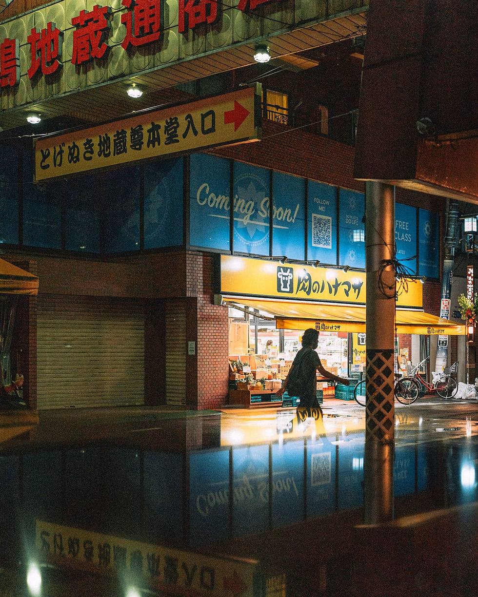 Thumbnail: A person riding a bicycle near shops with neon signs reflected in the wet pavement.