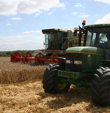 Harvest. John Deere tractor collecting grain from Claas combine harvester