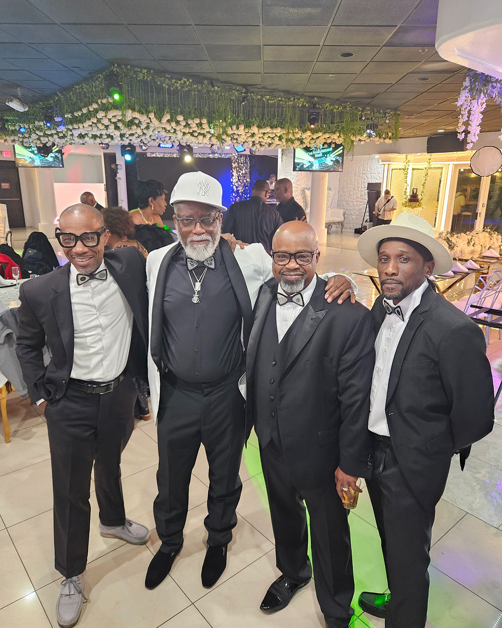 Four men in formal attire pose together at a decorated event venue.
