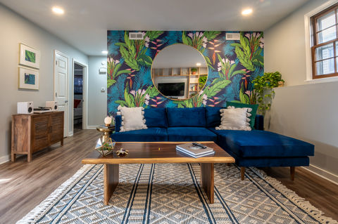 Photo of blue velvet sofa, infront of jungle theme wall paper with large round brass mirror.