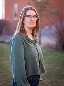 Photograph of Hannah Calder, from waist up, wearing green blouse and glasses with black rims. Hair long, to shoulders, light color.