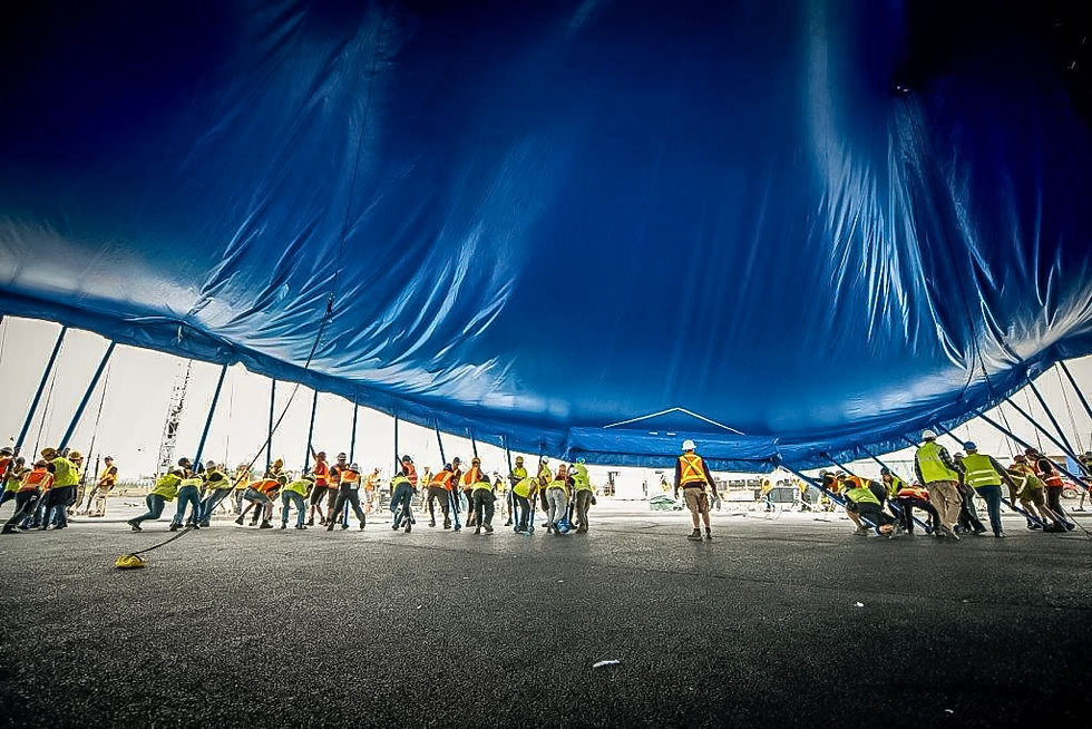 Een grote groep crewleden tilt samen een festivaltent omhoog, symbool voor teamwork en de One Crew-mentaliteit.