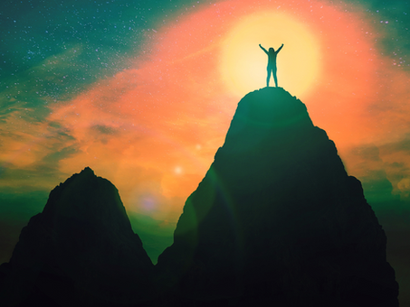 Person standing on top of a mountain with arms expanded to the sky.