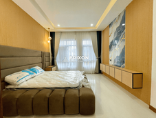 Bedroom with padded headboard wall and full-height window curtains.
