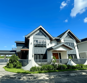 Elegant two-storey modern luxury house with a striking gabled roof, black and white façade, and landscaped front garden under a bright blue sky — an architectural masterpiece by Brixon Realty International in Pampanga.