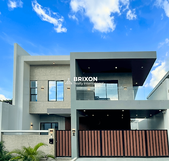 Modern two-story house with minimalist architecture, featuring a balcony with glass railing, black-and-wood gate, and clean geometric lines under a bright blue sky — Brixon Realty International.