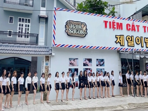 床屋の前に並ぶ多くの人々。背景に赤と黄色で「TIỆM CẮT TÓC JEIL」「제일 이발관」と書かれた看板。店の外観は青と赤のラインが特徴的。