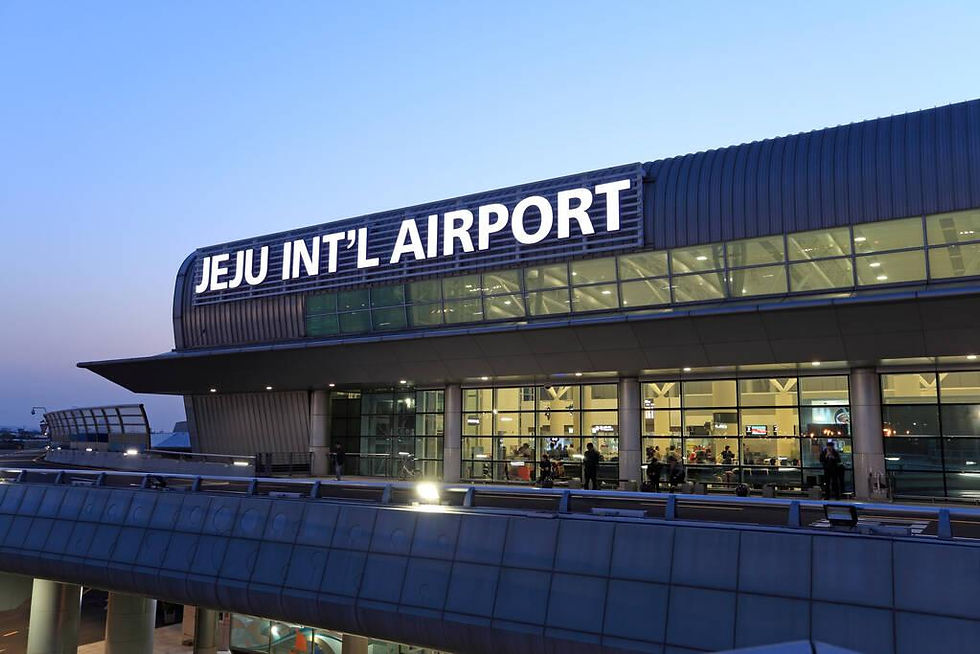 夕暮れの済州国際空港の外観。大きなJEJU INT'L AIRPORTの看板が光り、窓越しに人々が見える。