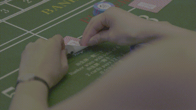 緑のグリッド柄の作業台で、腕時計をした手が小さな部品を並べている。白い文字が見え、集中した雰囲気。