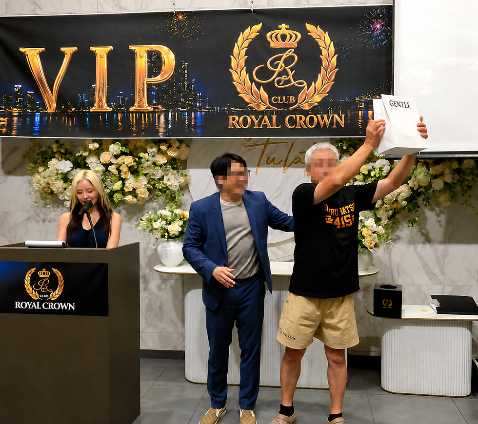 VIPロイヤルクラウンの会場で、女性が壇上で話し、男性2人が立つ。右の男性がGENTLEの袋を掲げ、華やかな花飾りとVIP看板が見える。
