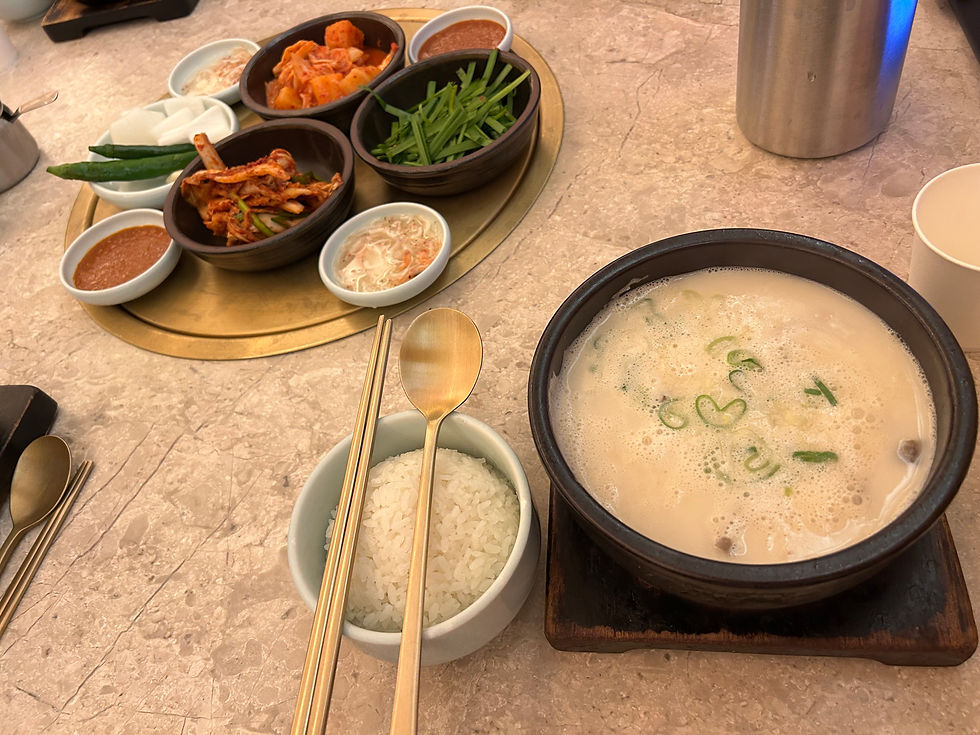 韓国料理の食卓。白いご飯とスープ、キムチやニラ、長ねぎ、ソースの小鉢が並び、石のテーブルに温かい雰囲気。
