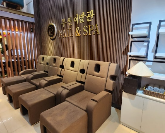 ブラウンのリクライニングチェアが並ぶ、木目調の壁に「NAIL & SPA」の文字がある店内。リラックスした雰囲気。
