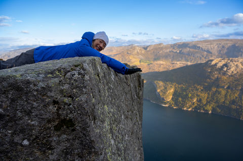 Hiker lying safely at the edge of Pulpit Rock with dramatic mountain and fjord scenery.