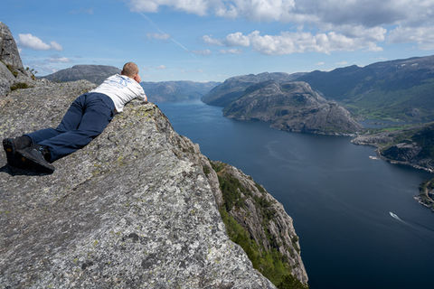 Hiker resting on a rock ledge with panoramic view over the Lysefjord during the guided hike to The Hat