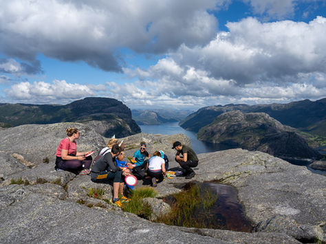 Small hiking group resting at the summit of The Hat with fjord views in the background