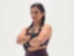 Woman with braids and black gloves poses confidently with crossed arms. Wearing maroon sportswear in a simple white studio. Tattoos visible.