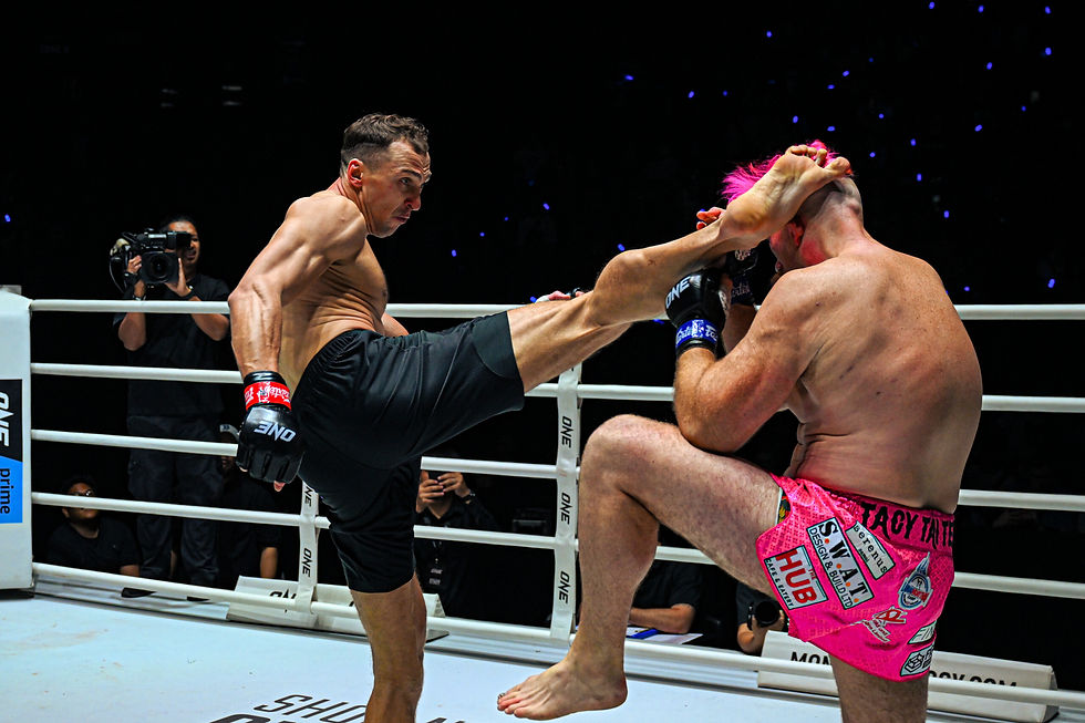 Two fighters clash in a ring; one delivers a high kick. The fighter in pink shorts blocks, camera crew in the background. Sporty atmosphere.